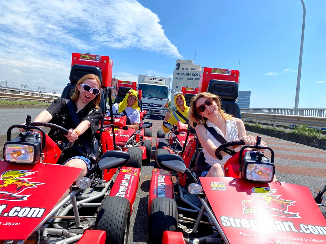 Group of friends riding red go-karts on a sunny highway, smiling at the camera with StreetKart branding on the vehicles.